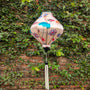 Lozenge shaped lantern with lotus flowers illustration cream silk fabric hanging against a brick wall with greenery
