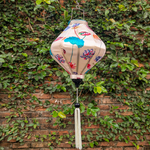 Lozenge shaped lantern with lotus flowers illustration cream silk fabric hanging against a brick wall with greenery