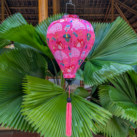 Pink Vietnamese silk lantern with tassel hanging among green leaves