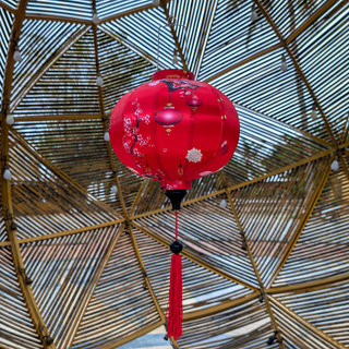 Red Vietnamese silk lantern with tassel hanging in front of the bamboo circus in Hoi An.
