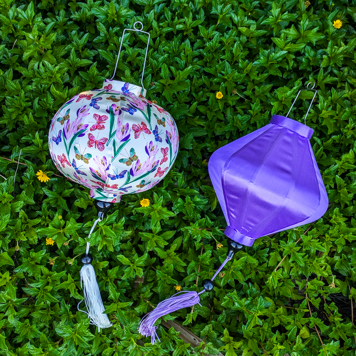 Decorative lanterns with floral design and purple shade on green foliage