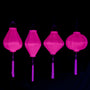 A row of hanging plain pink Vietnamese lanterns in Garlic, Tube, Lozenge and Round shapes glowing under UV light.