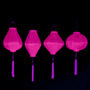 A row of hanging plain pink Vietnamese lanterns in Garlic, Tube, Lozenge and Round shapes glowing under UV light.