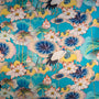 A repeating decorative pattern featuring large blue and pink lotus flowers, green leaves, and a white crane with black tail feathers on a bright turquoise background.