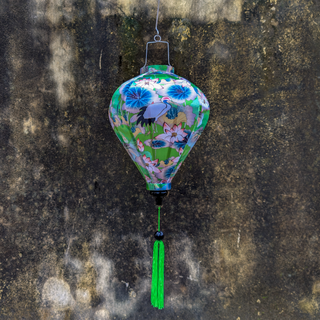 Balloon shaped Vietnamese silk lantern with Open Bill Birds and Lotus Flowers design and green tassel on a moldy textured wall.