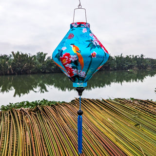 Lozenge shaped lantern outdoors with blue tassel and large orange birds on blue super silk fabric.