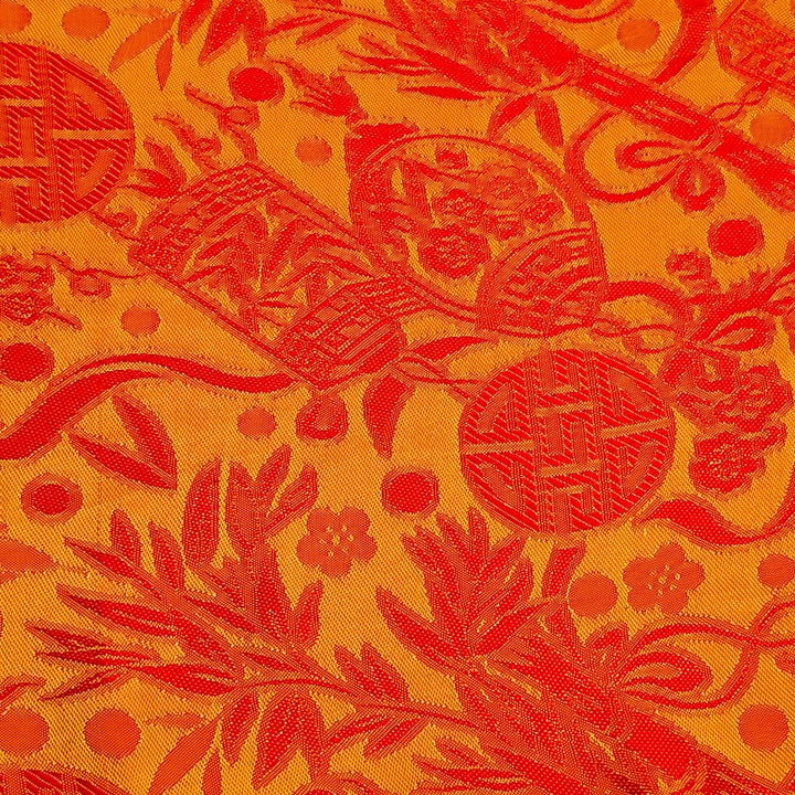 Close up of jacquard silk fabric with intricate patterns of flowers, bamboo, lanterns and symbols in two different shades of orange. 