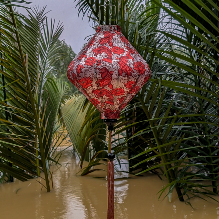 Orange koi against champagne gold Vietnamese silk lantern with matching champagne gold tassle hanging amidst green foliage and floodwaters.