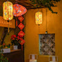 Glowing lanterns in cylinder and UFO shapes with cranes in flight surrounded by orange flowers on a bright yellow background at a cafe in Old Town Hoi An.