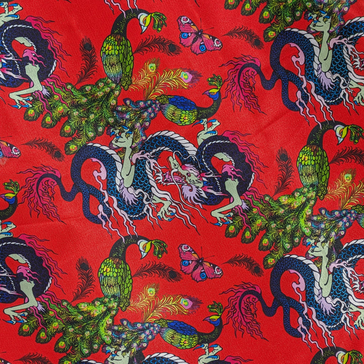 Close up of polyester silk fabric adorned with intricate prints of dragons, peacocks, and butterflies against a striking red background.