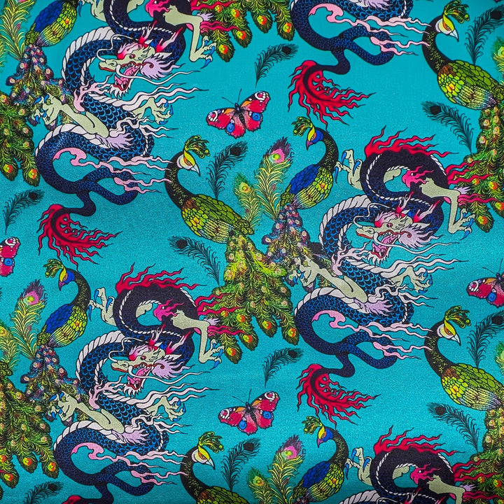 Close up of polyester silk fabric with flamboyant peacocks, butterflies and dragons against a striking blue background.