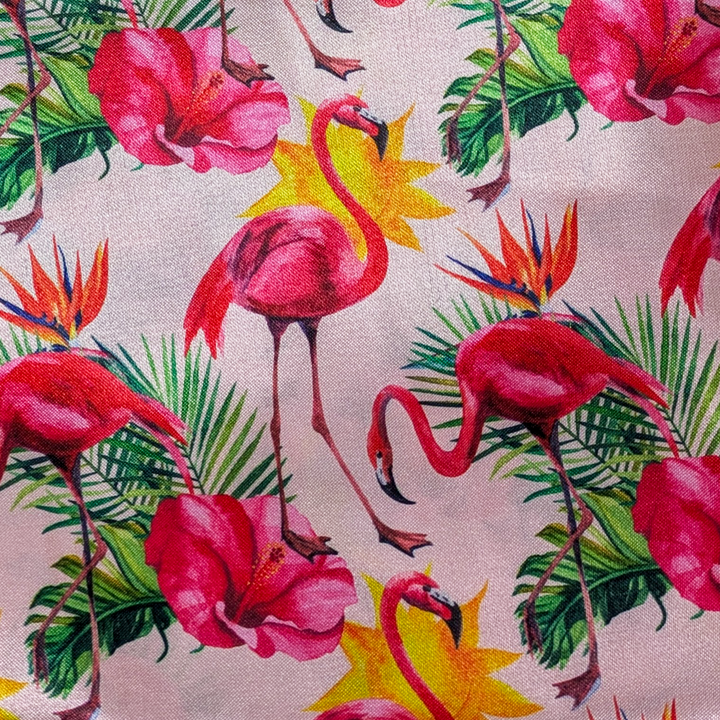 Close up of polyester silk fabric with a print of hot pink flamingos and flowers such as including bird of paradise flowers on a light pink background.