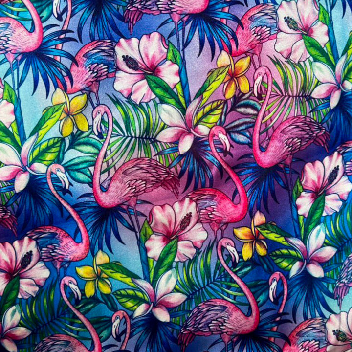 Polyester silk fabric with a print of pink flamingos, hibiscus, and frangipani flowers on a blue background. 