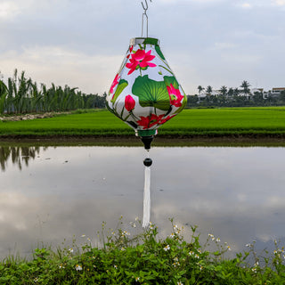 Teardrop shape Vietnamese silk lantern with white tassel and fabric with a print of bright pink lotus flowers against a white background.