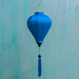 Balloon shaped blue plain silk Vietnamese lantern in front of an aging blue wall in Old Town, Hoi An.