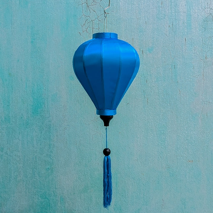 Balloon shaped blue plain silk Vietnamese lantern in front of an aging blue wall in Old Town, Hoi An.