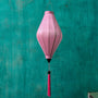 Tube shaped Vietnamese lantern in light pink plain silk with a bright pink tassel hanging in front of a bright blue wall.