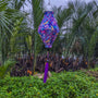 Balloon shaped lantern with purple tassel featuring a paisley print hanging in the front of palm trees and a river.