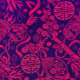 Close up of jacquard silk fabric with intricate patterns of bamboo, lanterns and symbols in red against dark purple background.