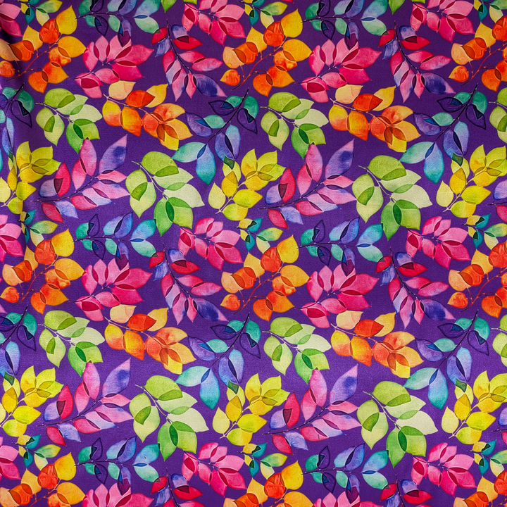 A close up of polyester silk fabric with green, pink, purple, orange, yellow leaves set against a rich purple background. 