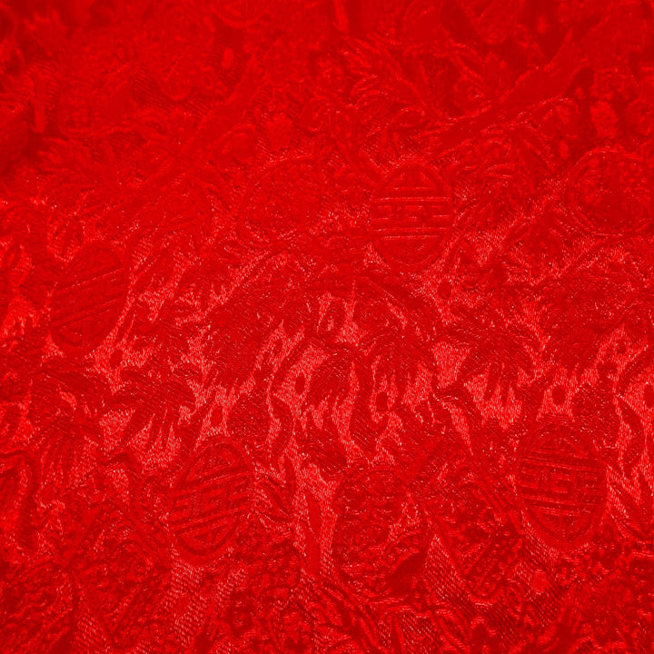 Close up of jacquard silk fabric with intricate patterns of flowers, bamboo, lanterns and symbols in red colour.