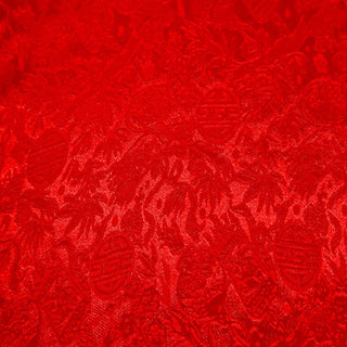 Close up of jacquard silk fabric with intricate patterns of flowers, bamboo, lanterns and symbols in red colour.