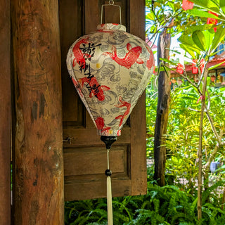 Balloon shaped lantern with red koi fish design hanging against a wooden background with greenery.