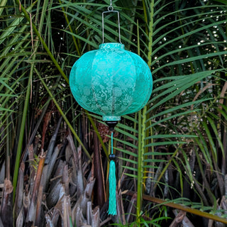 Sea green / turquoise Vietnamese Jacquard silk lantern with matching tassel hanging among palm trees