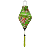 A lantern in a tube shape with a print of swallow birds in a cherry tree with red and pink blossoms on a green background with a green tassel.