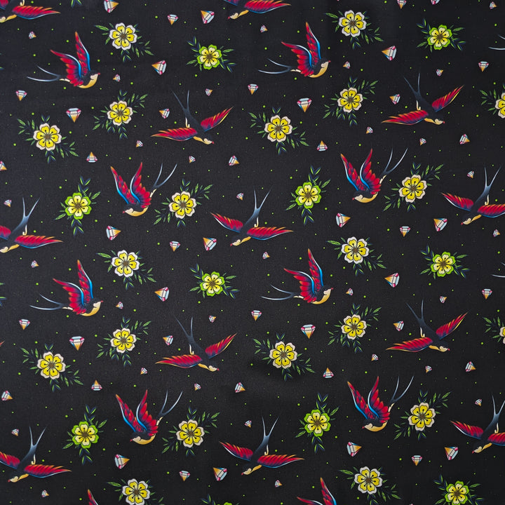 Polyester silk fabric with a print of flying swallows with striking red and blue wings set against a bold black backdrop adorned with diamonds and yellow daisy flowers. 