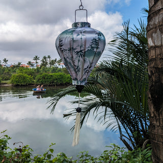 Balloon shaped Vietnamese lantern with a print of pagodas and temples above misty hilltops with large bamboo trees in the wild with people traveling up the river in a coconut basket.