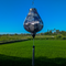 Garlic shaped lanterns featuring a print of mountains, trees, temples, men in boats, and large rocks. A beautiful palette of light pinks and purples against a serene creamy background hanging in front of lush green rice fields and blue open skies.