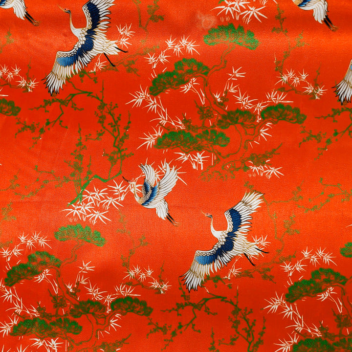 Vibrant orange polyester silk fabric adorned with elegant cranes and lush tree patterns, used to handcraft lanterns in Hoi An.
