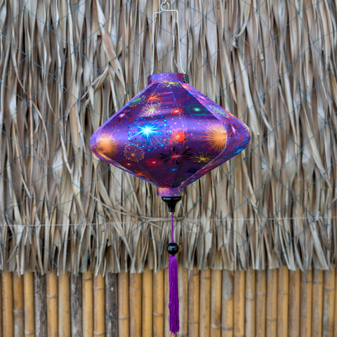 Decorative purple lantern with in UFO shape with star pattern hanging against a thatched wall.