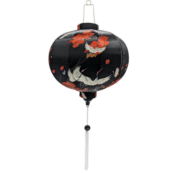 Round Vietnamese silk lantern with white tassel featuring a print of swooping white cranes and falling orange flowers against black backdrop.