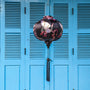 Round shaped Vietnamese Hoi An lantern featuring red-headed white cranes amongst pink cherry blossoms against a black background hanging in front of blue shutters. Perfect for home decor.