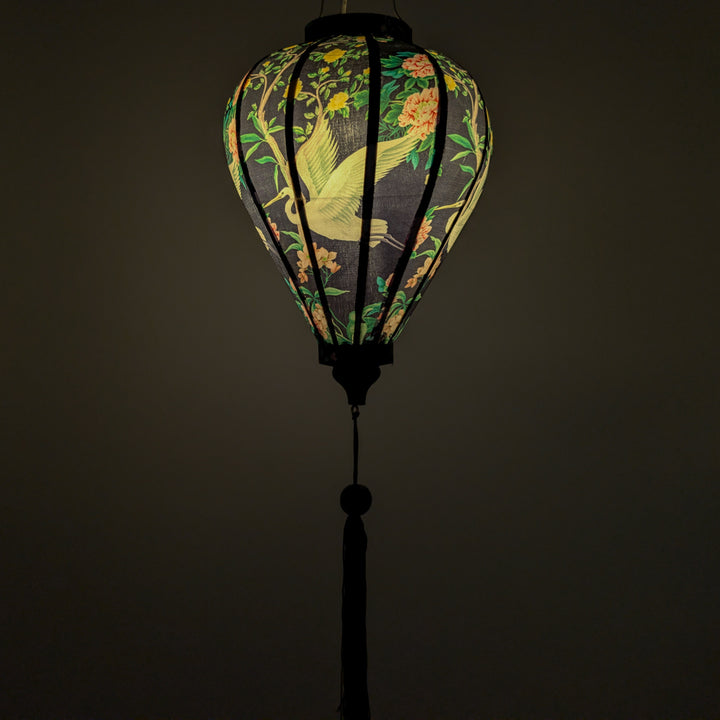 Glowing silk lantern with floral and bird design on a black background