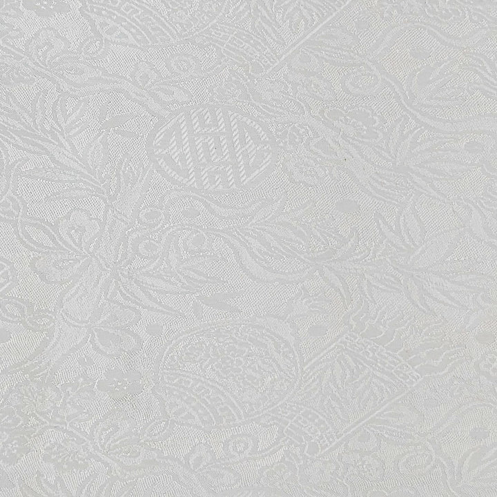 Close up of white jacquard silk fabric with intricate patterns of bamboo, lanterns and symbols.