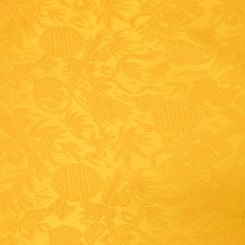 Close up of jacquard silk fabric with intricate patterns of flowers, bamboo, lanterns and symbols in a bright yellow colour.