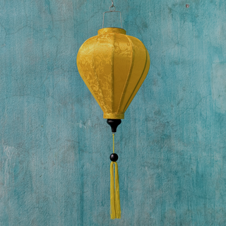 Yellow Jacquard silk lantern in a balloon shape with matching yellow tassel hanging in front of a textured blue wall