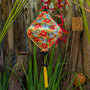Lozenge shaped lantern with yellow and orange daisies hanging among plants and wooden planks in a garden