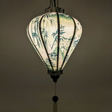 Glowing Balloon shaped Vietnamese lantern with a print of pagodas and temples above misty hilltops with large bamboo trees on white background.