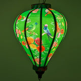 Glowing up close of Balloon shaped lantern with green tassel featuring a print of bright bunches of flowers and various feathery avian species on a bright green backdrop.