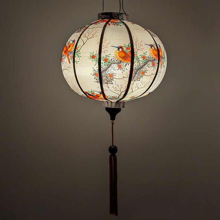 Glowing Vietnamese silk lantern handmade in Hoi An with bird and floral patterns on a white background.