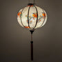 Glowing Vietnamese silk lantern handmade in Hoi An with bird and floral patterns on a white background.