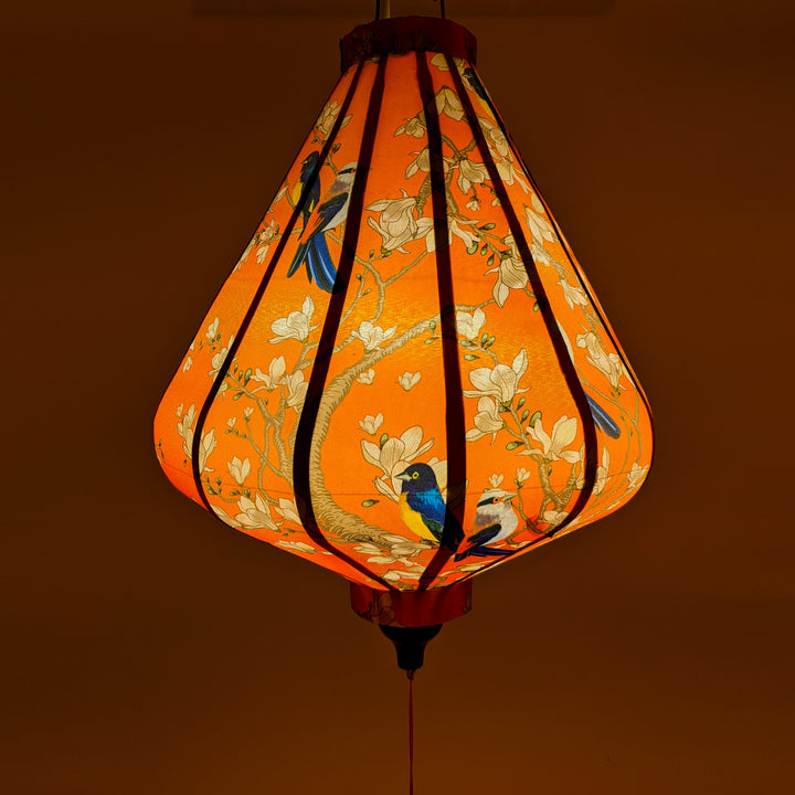 Teardrop Vietnamese silk lantern with glowing orange hue with a print of bluebirds perched on a tree amidst white flower blossoms.