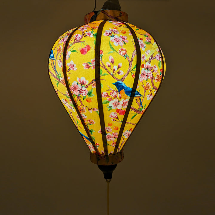 Balloon shaped Vietnamese Lantern featuring a blue and orange bird sitting on a branch in a cherry tree with a cosy yellow glow.