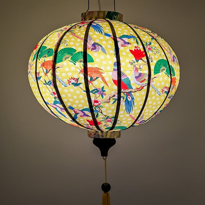 Glowing round Vietnamese silk lantern with colourful bird design on a yellow background