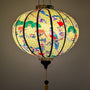 Glowing round Vietnamese silk lantern with colourful bird design on a yellow background