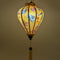 A beautifully illuminated yellow Hoi An silk lantern adorned with intricate blue cranes, delicate pink cherry blossoms, and festive red lantern motifs. The warm glow enhances the elegance of the hand-painted details, while the traditional wooden frame and golden tassel add a classic touch. This lantern brings a cozy ambiance, perfect for home decor, cultural celebrations, or thoughtful gifts.